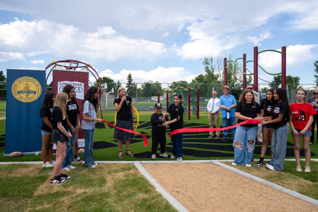 A ribbon-cutting ceremony at a playground, featuring students and guests, celebrating a new school facility.