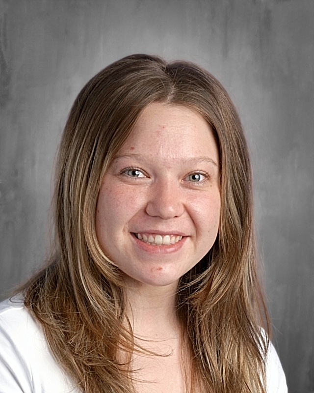 Smiling young woman with long, light brown hair, wearing a white shirt, against a gray background.