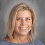 Smiling woman with blonde hair and blue eyes, wearing a gray top, set against a neutral background.