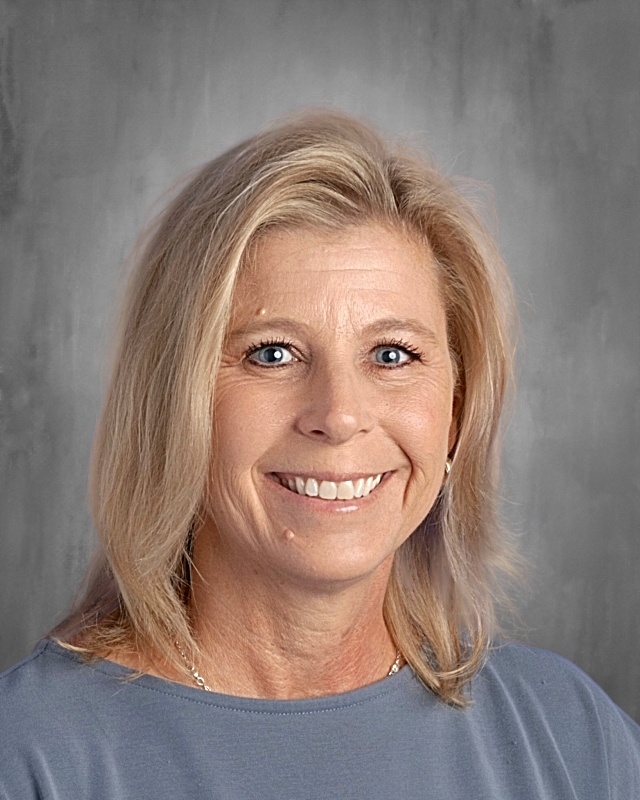Smiling woman with blonde hair and blue eyes, wearing a gray top, set against a neutral background.