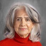 Senior woman with long, wavy gray hair wearing a red turtleneck sweater, smiling against a neutral background.