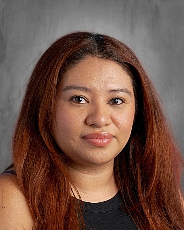 Close-up portrait of a woman with long, wavy brown hair, wearing a black top, against a gray background.
