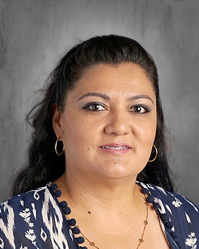 Portrait of a woman with long dark hair, wearing a patterned top and earrings, set against a gray background.